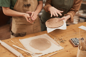 Warm toned close up of two young people making ceramics while working at pottery workshop, small...