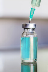 Vial filled with liquid vaccine in medical lab with syringe. medical ampoule and syringe on the glass surface
