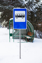 Bus stop in the middle of a beautiful winter road in the middle of the forest with a bus stop sign.