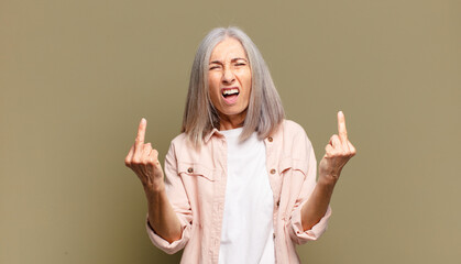 senior woman feeling provocative, aggressive and obscene, flipping the middle finger, with a...