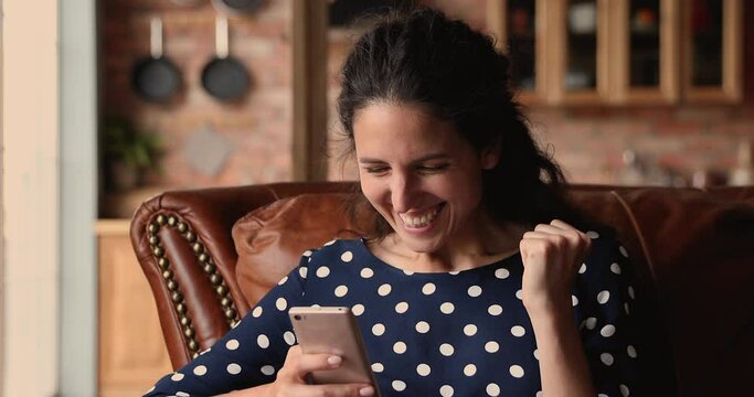 Young female sit on couch holding smart phone feels overjoyed of getting shopping promo code of internet web store, celebrate amazing unbelievable news, online lottery win, dating invitation concept