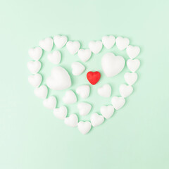 Heart shape made of white hearts and one red heart on pastel green background. Minimal love Valentines or Mother's day aesthetic. Flat lay.