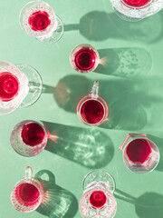 Glasses of red drinks with sunlit shadows on green background. Creative summer party concept.  Flat lay.