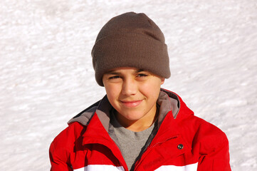 Portrait of a young boy wearing parka and ski cap with snow background. © Steve Cukrov