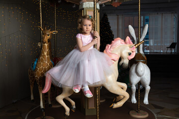 a little girl in a pink dress and a crown on a carousel with a white pony