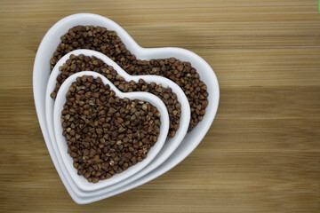 Buckwheat in a heart-shaped bowl on a wooden background.