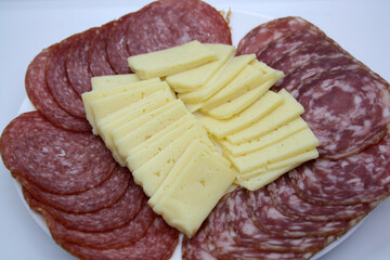Salami slices and cheese on a white plate.