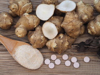 Fruits of the Jerusalem artichoke plant, pills and natural powder with inulin on a  wooden table, top view. Healthy helianthus tuberosus root vegetables and dietary supplements for diabetes prevention