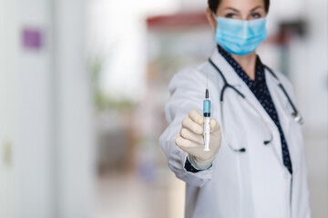 Doctor shows syringe with vaccine on blurred background.
