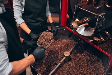 Two baristas enjoying burned beans aroma while holding them on spatula. Industry concept. Close up...