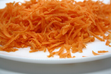 Grated orange carrots on a white plate. Background.