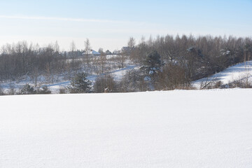 A rural landscape in the winter season, full of deep, fluffy snow. Trees without leaves. Large snowdrifts in agricultural fields in Poland.