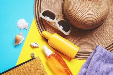 Travel sunscreen spray and moisturizing body cream, straw hat, sunglasses, cosmetic bag and towel. Flat lay summer beauty photography beach essentials