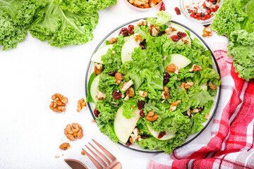 Kale salad with dried cranberry, green apples and walnuts. Healthy vegan food, top view, grey kitchen table background