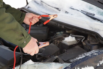 White hands connects the red and blackterminals on frozen car engine, quick start with spare...