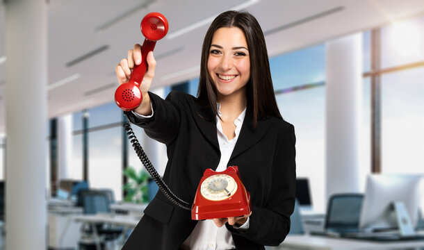 Young female manager holding a red vintage phone, contacs us concept