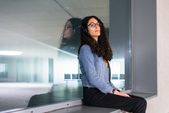 Transgender woman with afro hair sitting and leaning on a window from where her reflection can be seen.