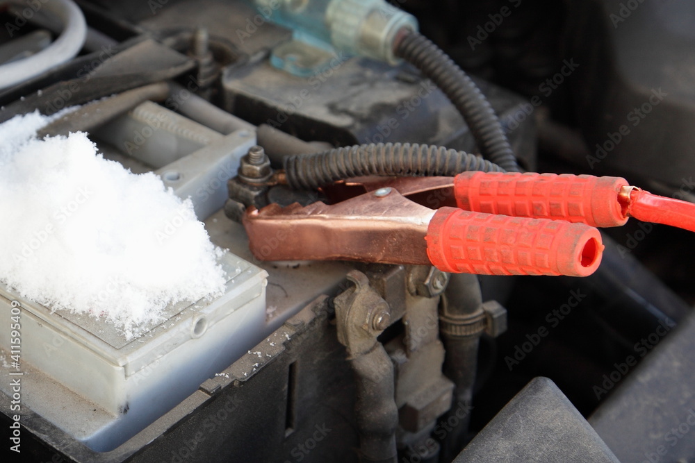 Wall mural Car engine starting wire red alligator terminal on cold snowy car battery positive pin close up, Quick start vehicle motor on a winter frost 