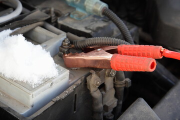 Car engine starting wire red alligator terminal on cold snowy car battery positive pin close up,...