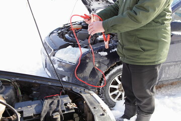 The man starts the car engine with the starting wires with crocodile clips from another vehicle,...