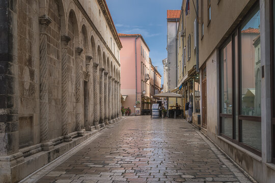 Fototapeta Tourists dining in outdoor restaurants in narrow streets of the old town district, surrounded by ancient Romanesque architecture, Zadar, Croatia