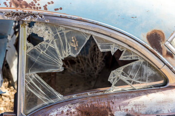 Pieces of safety glass create a shattered frame showing tumbleweed inside of a rusty old car