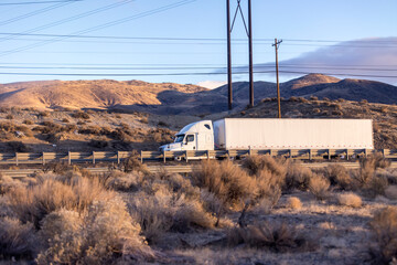 White anonymous semi truck drives down remote desert highway beneath power lines