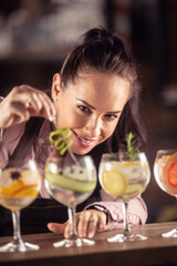 Bartender loving her job decorates gin tonic cocktails in glasses on a bar