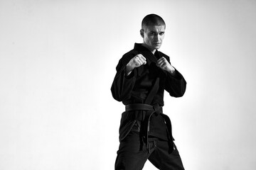 Confident male in kimono fighter posing in karate stance on studio background with copy space, black and white portrait © Georgii