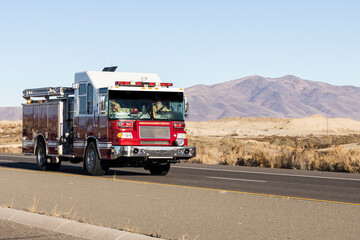 Red and white fire truck driving down a road in the desert responding to an emergency call - Powered by Adobe