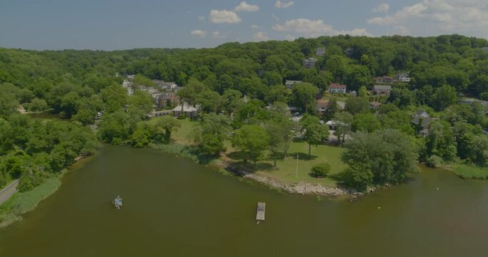 Flying Over Anchored Boats on Harbor and Towards Houses Amongst Trees