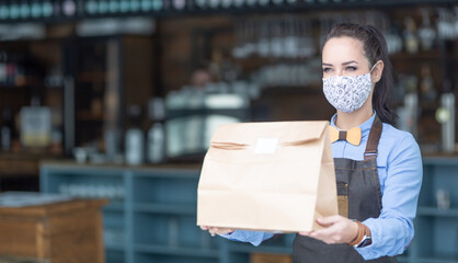 Restaurant employee hands over food packed in a paper bag wearing face mask during Covid-19 pandemic