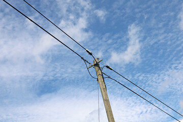 Old wooden power pole with power lines against blue cloudy sky