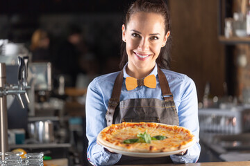Waitress smiles while serving large authentic Italian pizza in a restaurant