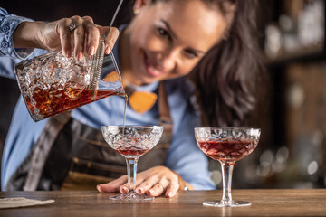 Female bartender pours manhattan cocktail into an ornamental glass