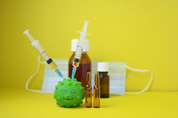The concept of vaccination or coronavirus is depicted using a rubber toy fish with two syringes and drugs stuck in the body on a yellow background with copy space.