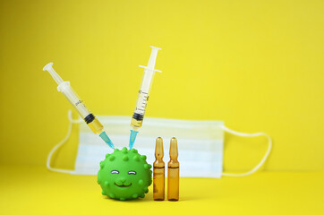 The concept of vaccination or coronavirus is depicted using a rubber toy fish with two syringes and drugs stuck in the body on a yellow background with copy space.