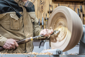 Turning wooden bowls on a lathe. The close up view of spinning the lathe machine. Man with a chisel and shavings flying off. - 411600400