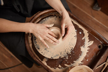 High angle closeup of elegant female hands shaping clay on pottery wheel in workshop while enjoying arts and crafts, copy space