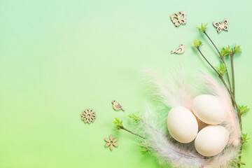 White Easter eggs in a delicate nest of colored feathers with unfurled leaf buds on the branches. Spring, a religious holiday, the birth of life. Copy space. Pale green background
