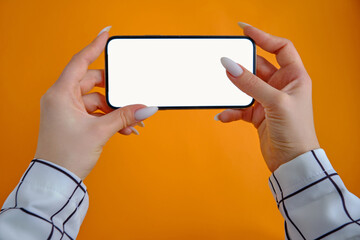 Phone with a blank white clean screen for product presentation in the hands of a girl on an orange background