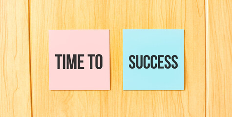 Inscription TIME TO SUCCESS on pink and blue square sticky sticker on wooden wall