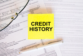 Yellow sticker with text Credit History on financial docs. Notepad, eyeglasses and white pen