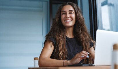 Smiling caucasian woman working on laptop and looking happy. Freelancer using computer, networking...