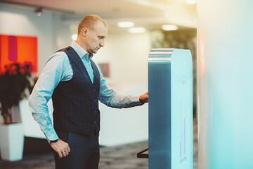 An adult serious man entrepreneur is interacting with a modern electronic terminal in the office; a...