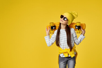 cool hipster little child girl in sunglasses posing with yellow skateboard on studio background. copy space