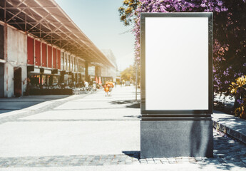 A street mockup of a blank advertising poster on the sidewalk near a shopping mall; an empty vertical outdoor banner template; billboard placeholder mock-up on a city boulevard on a warm bright day