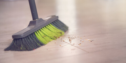 Colored broom stands on wooden floor next to pile of debris and dust.