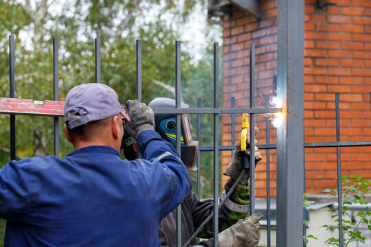A team of construction workers install a metal fence around a new home.