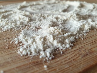 Close-up in perspective of a pile of flour on a wooden board.  Background image for cooking themes, recipe preparation, cookbooks.